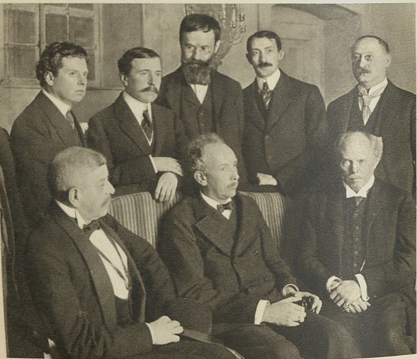 Black-and-white group photo of eight men in suits, seated and standing in a room, the team behind the 1911 Der Rosenkavalier premiere
